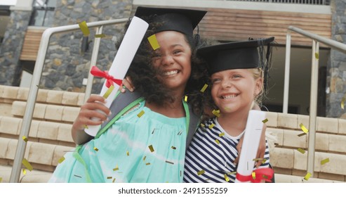 Image of gold confetti over happy diverse schoolgirls with diplomas and mortar boards embracing. Achievement, graduation, school, childhood, education and learning, digitally generated image. - Powered by Shutterstock