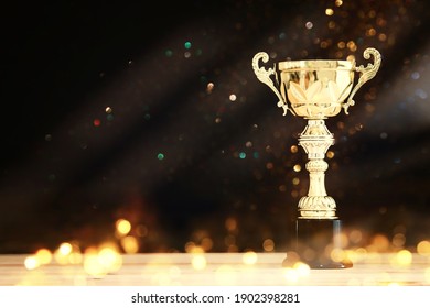 image of gold trophy over wooden table and dark background, with abstract shiny lights
