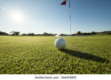 Image Of A Golf Ball On Green Shot From A Low Angle And Close To Flag