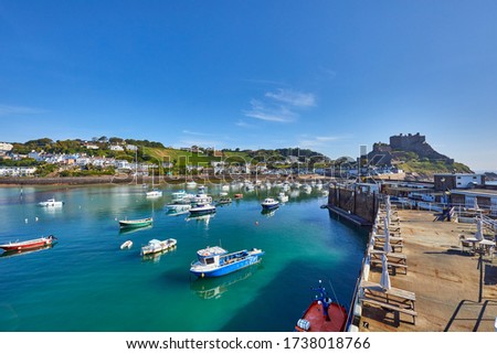 Image of Gorey Harbour with fishing and pleasure boats, the pier bullworks and Gorey Castle in the background with blue sky. Jersey, Channel Islands, UK