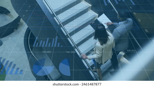 Image of graphs, changing numbers, overhead view of diverse coworkers discussing reports. Digital composite, multiple exposure, business, growth, planning and teamwork concept.