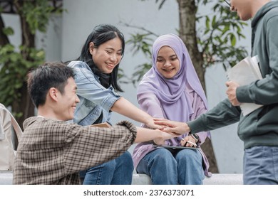 Image of a group of cheerful Asian college students putting their hands together, showing teamwork and unity. - Powered by Shutterstock