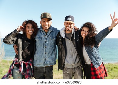 Image Of A Group Of Happy African Friends Walking Outdoors On The Beach. Looking At Camera Showing Peace Gesture.