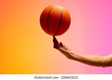 Image of hand of biracial basketball player spinning basketball on pink to orange background. Sports and competition concept. - Powered by Shutterstock