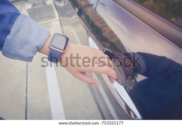 Image\
of a hand grabbing a car\'s door with a smart watch on the wrist.\
Mock up. Technology. Background go a parking\
lot.