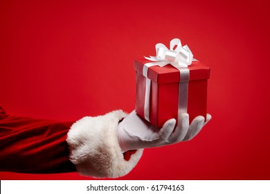 An Image Of Santa?s Hand Holding A Gift Box Against Red Background