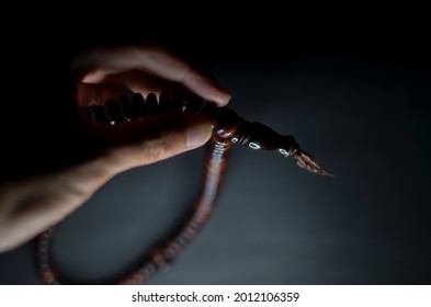An image of hand holding a Muslim Tasbih Prayer Beads Palm Seeds Islamic Prayer Zikr Misbaha isolated with black background.