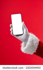 Image of hand of santa claus holding smartphone with blank screen and copy space on red background. Christmas, connection, technology, tradition and celebration concept.