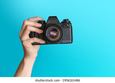Image of hand with vintage camera on empty blue background.