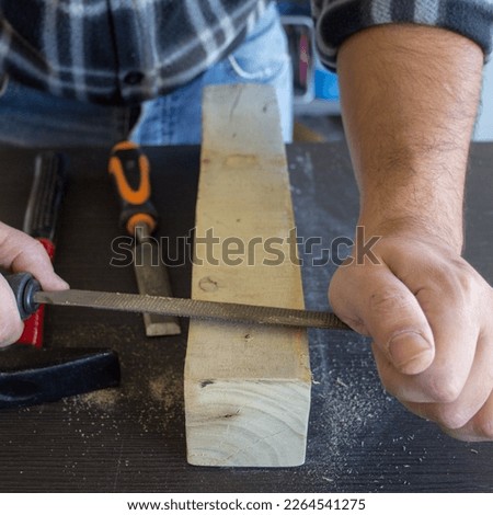 Image of the hands of a carpenter craftsman who smoothes a piece of wood with a rasp. Wood filing and cleaning.
