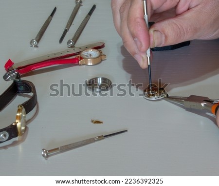 Image of the hands of a goldsmith who repairs a small wristwatch with the tools of the trade. Watchmaker at work.
