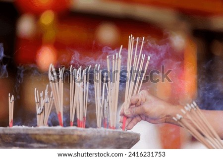 Image of hands placed several lit incense sticks into a pot that can hold the ash from the burn incense sticks. It is a place to pay homage to sacred things according to beliefs specific person.
