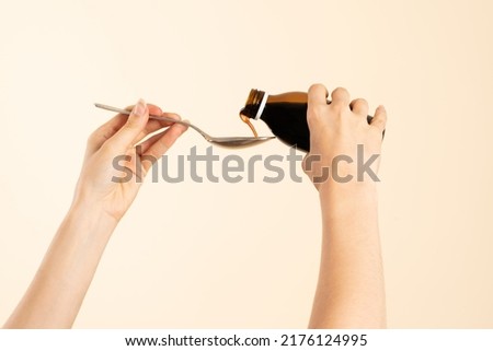 Image of hands with table spoon and bottle of medication. Pouring cough syrup or cold liquid medication into spoon. Bottle with no label.