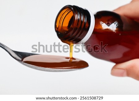 Image of hands with table spoon and bottle of medication. Pouring cough syrup or cold liquid medication into spoon. Bottle with no label.
