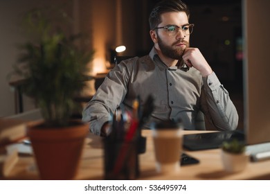 Image Of Handsome Bearded Web Designer Dressed In Shirt Working Late At Night And Looking At Computer.