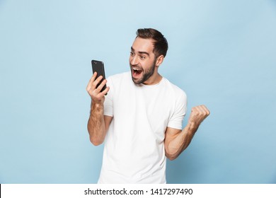 Image Of A Handsome Excited Young Man Using Mobile Phone Isolated Over Blue Wall Background Make Winner Gesture.