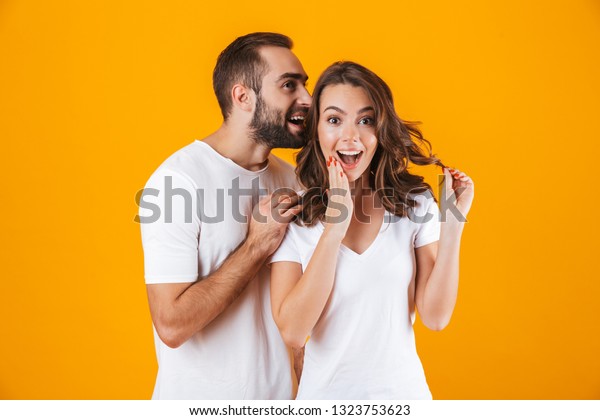 Image of handsome\
man whispering secret or interesting gossip to woman in her ear\
isolated over yellow\
background