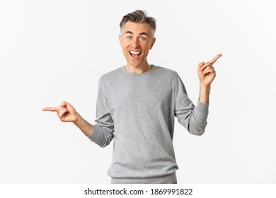 Image of handsome middle-aged man in grey sweater, showing two variants, pointing fingers sideways, demonstrating left and right copy space, standing over white background - Shutterstock ID 1869991822