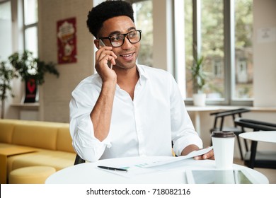 Image of handsome young african man sitting coworking with documents talking by phone. Looking aside. - Powered by Shutterstock