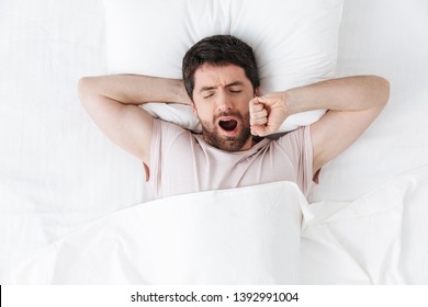 Image of a handsome young man in the morning yawning and stretching in bed. - Powered by Shutterstock