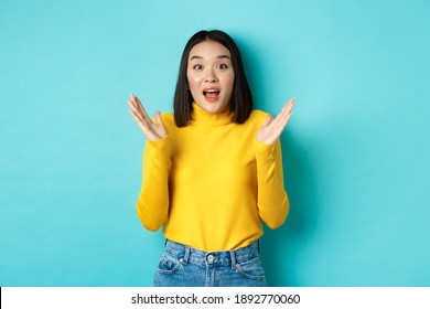 Image Of Happy Asian Woman Clap Hands And Looking Amazed, Standing In Yellow Pullover Over Blue Background