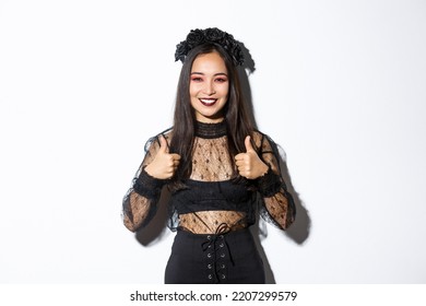 Image Of Happy Asian Woman In Halloween Party Dress Showing Thumbs-up In Approval. Girl Wearing As Witch Or Widow Looking Pleased, Like Or Agree With Something, White Background