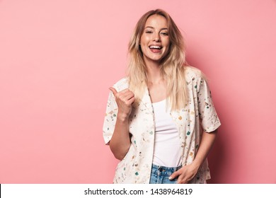 Image of happy beautiful blonde woman posing isolated over pink wall background showing copyspace pointing.