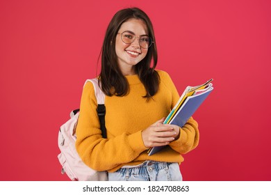 Imagen de una feliz y bella estudiante posando con libros de ejercicios aislados sobre fondo rosa