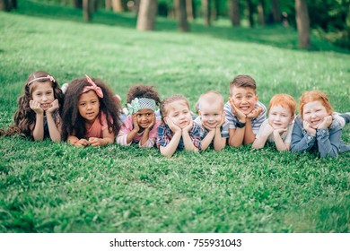 Image Of Happy Boys And Girls Lying On A Green Grass. The Concept Of Friendship, Childhood And Intercultural Communication. Children Lie On The Grass Substituting The Hands Under The Head.