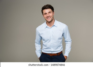 Image of happy brunette man wearing formal clothes smiling at camera with hands in pockets isolated over gray background