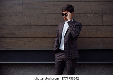 Image Of Happy Brunette Man Wearing Formal Clothes, Serious Facial Expression Looking Not At Camera With Hands In Pockets On Brown Plates Background.