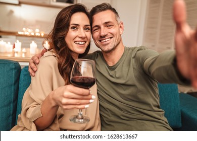 Image Of Happy Caucasian Couple Taking Selfie Photo While Having Romantic Candlelight Dinner At Home