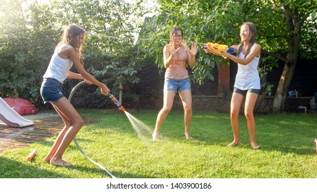 Image Of Happy Children Having Water Gun Fight At House Backyard Garden. Family Playing And Having Fun Outdoors At Summer