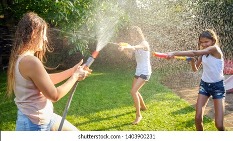 Image Of Happy Children Having Water Gun Fight At House Backyard Garden. Family Playing And Having Fun Outdoors At Summer