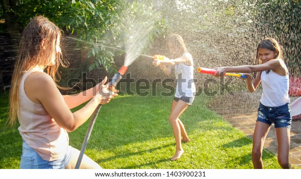 Image of\
happy children having water gun fight at house backyard garden.\
Family playing and having fun outdoors at\
summer