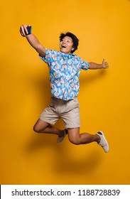 Image Of Happy Emotional Young Asian Man Jumping Isolated Over Yellow Background Take A Selfie By Mobile Phone.