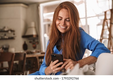 Image of happy ginger woman smiling and using mobile phone while sitting at cozy kitchen - Shutterstock ID 1793292766