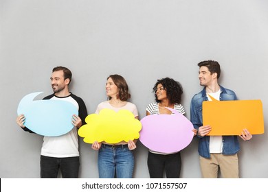 Image of happy group of friends standing isolated over grey wall background holding speech and thoughtful bubbles. - Shutterstock ID 1071557507