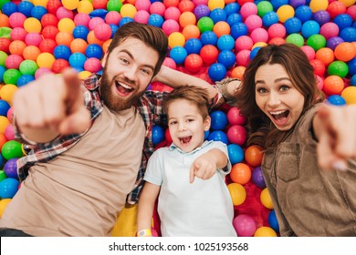 Image of happy little child have fun with his parents in entertainment game center pointing to camera.