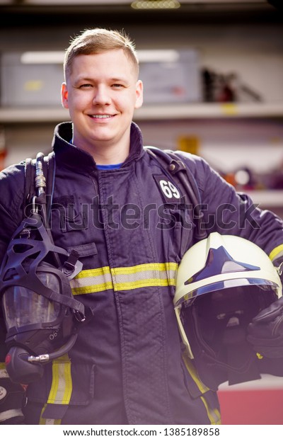 Image of happy male firefighter\
with helmet in his hands against background of fire\
truck