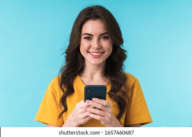 Image of a happy optimistic young pretty woman posing isolated over blue wall background using mobile phone.