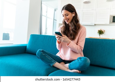 Image of a happy optimistic young woman sit indoors at home using mobile phone on sofa.