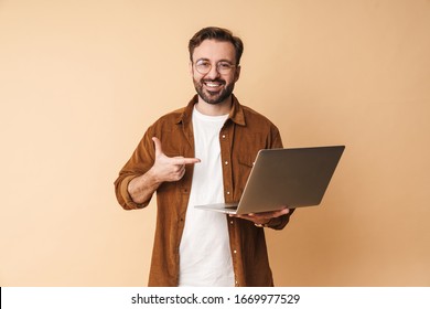 Image of a happy positive young unshaved man isolated over beige wall background using laptop computer pointing. - Shutterstock ID 1669977529