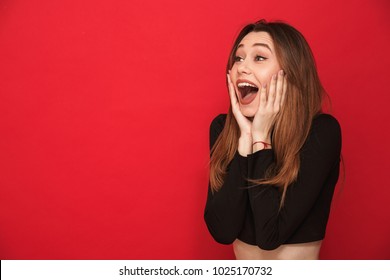 Image of happy screaming surprised young woman standing isolated over red background. Looking aside.