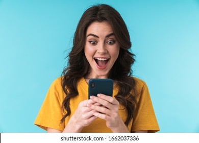 Image of a happy surprised shocked young pretty woman posing isolated over blue wall background using mobile phone.