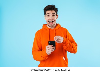 Image Of A Happy Surprised Young Bristle Man Isolated Over Blue Wall Background Using Mobile Phone.