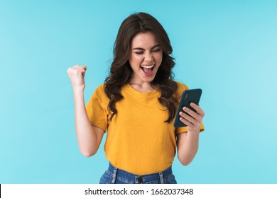 Image of a happy surprised young girl isolated over blue wall background using mobile phone make winner gesture. - Powered by Shutterstock