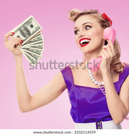 Image of happy woman with money, talking on phone, pin-up style dress in polka dot, over pink background. Caucasian blond model posing in retro fashion and vintage studio shoot.