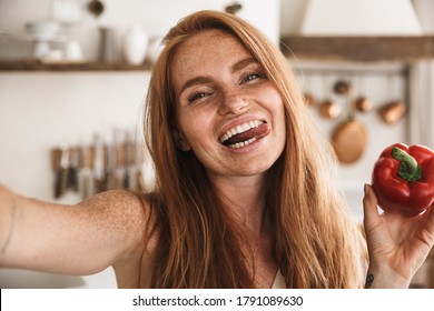 Image Of Happy Woman Taking Selfie Photo On Mobile Phone With Bell Pepper While Cooking At Cozy Kitchen