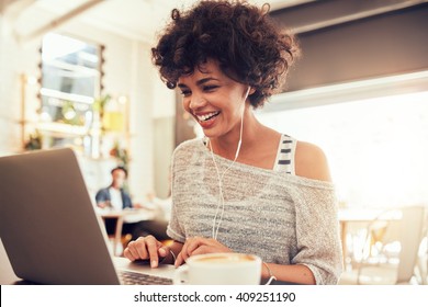 Image of happy woman using laptop while sitting at cafe. Young african american woman sitting in a coffee shop and working on laptop. - Powered by Shutterstock